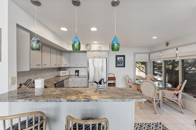 kitchen with stainless steel appliances, kitchen peninsula, pendant lighting, decorative backsplash, and a breakfast bar