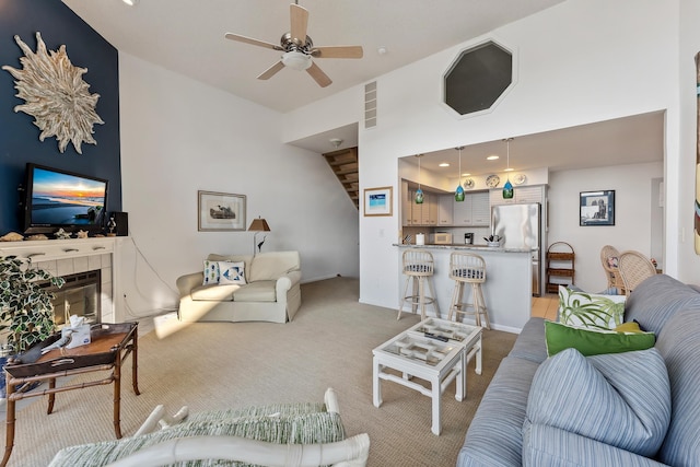 living room with ceiling fan, light colored carpet, a towering ceiling, and a fireplace