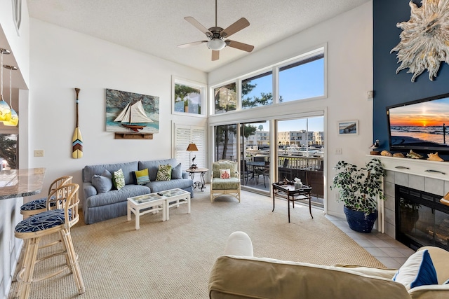 living room with a tile fireplace, ceiling fan, light tile patterned floors, a towering ceiling, and a textured ceiling