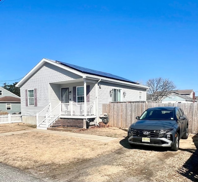 view of front of house with covered porch, roof mounted solar panels, and fence