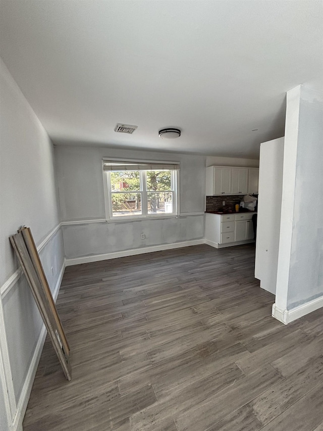 unfurnished living room with dark wood-style flooring, visible vents, and baseboards