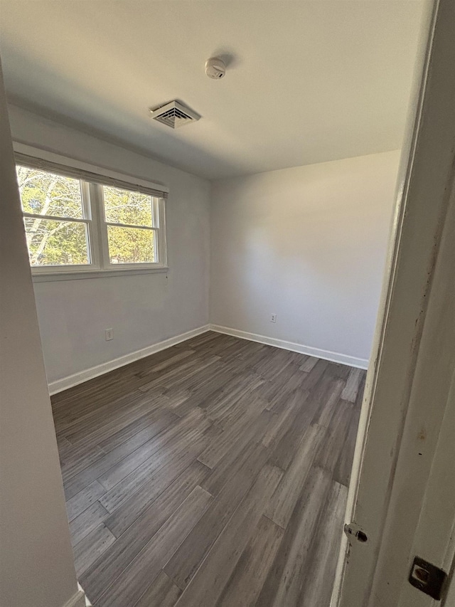 spare room with dark wood-style floors, visible vents, and baseboards