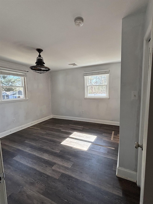 empty room featuring a healthy amount of sunlight, baseboards, and dark wood finished floors