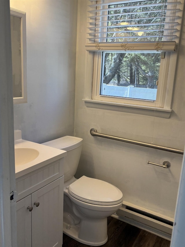 half bathroom featuring a baseboard heating unit, vanity, toilet, and wood finished floors