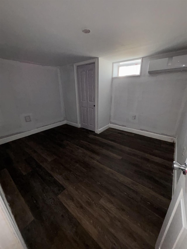 interior space featuring dark wood-style floors, an AC wall unit, and baseboards