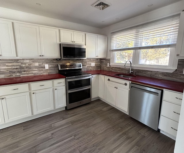 kitchen featuring stainless steel appliances, dark countertops, visible vents, backsplash, and a sink