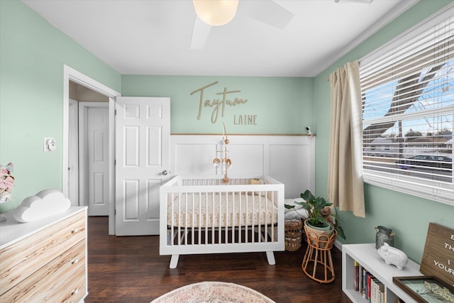 bedroom featuring dark wood-type flooring, ceiling fan, and a crib