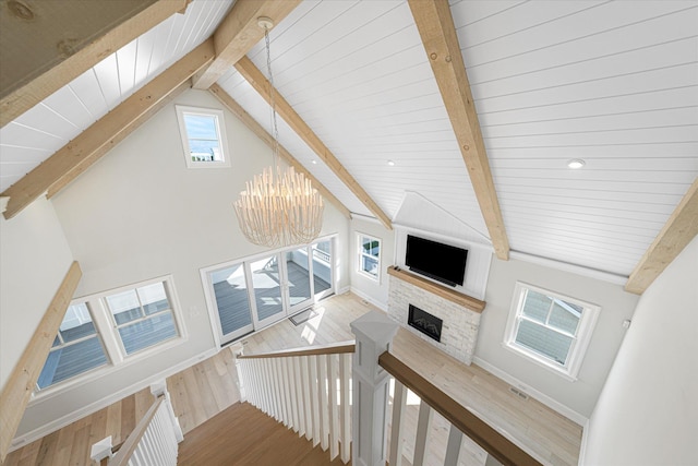 staircase featuring beam ceiling, wooden ceiling, a stone fireplace, a notable chandelier, and wood-type flooring