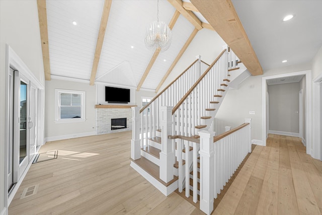 stairs featuring a brick fireplace, lofted ceiling with beams, an inviting chandelier, and wood-type flooring