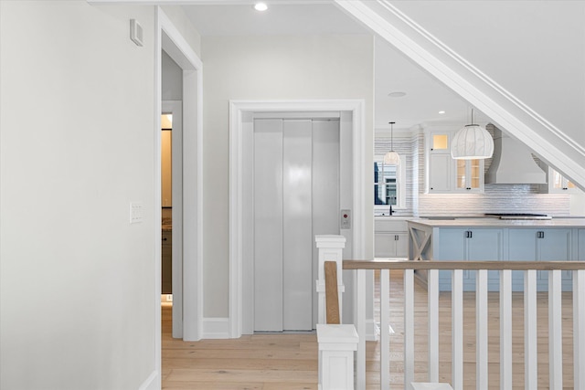 kitchen with elevator, white cabinetry, wall chimney exhaust hood, hanging light fixtures, and backsplash