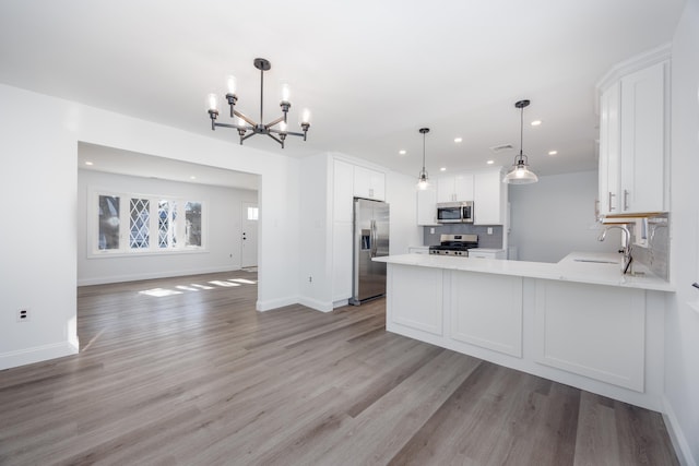 kitchen with pendant lighting, appliances with stainless steel finishes, kitchen peninsula, and white cabinets