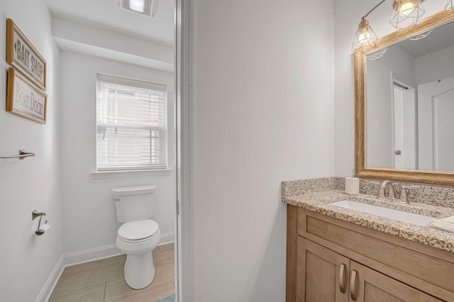 half bathroom featuring wood finished floors, vanity, toilet, and baseboards