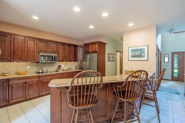 kitchen featuring a kitchen bar, stainless steel appliances, a kitchen island, and light stone countertops