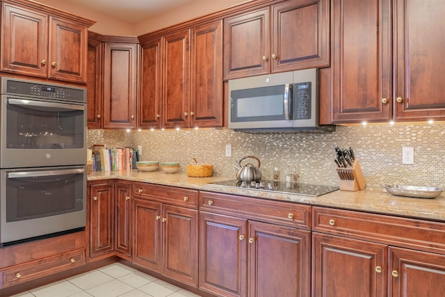 kitchen featuring tasteful backsplash, light stone counters, light tile patterned floors, and appliances with stainless steel finishes