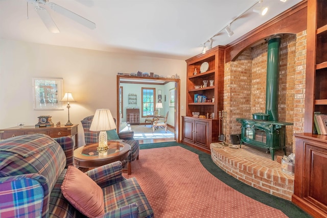 living room featuring carpet flooring, ceiling fan, a wood stove, and rail lighting