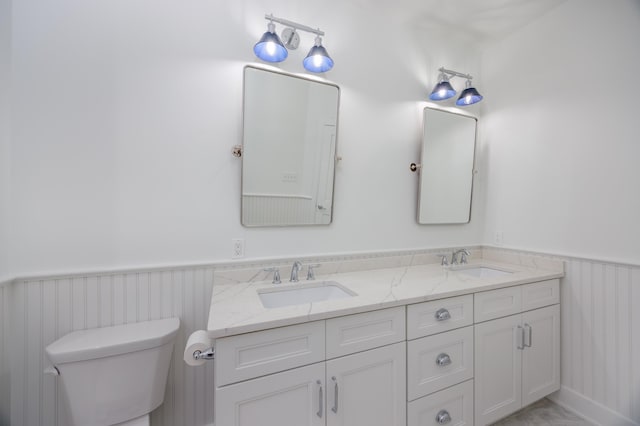 full bathroom with double vanity, toilet, wainscoting, and a sink