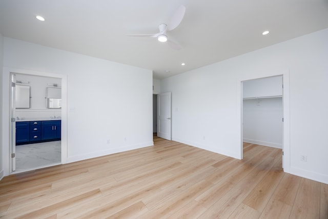 unfurnished bedroom with a walk in closet, baseboards, light wood finished floors, connected bathroom, and recessed lighting