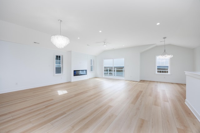 unfurnished living room with a glass covered fireplace, light wood finished floors, a healthy amount of sunlight, and lofted ceiling