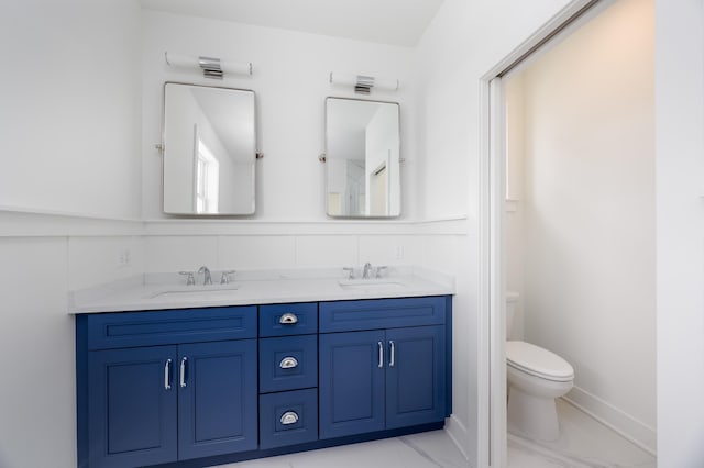 bathroom featuring double vanity, toilet, a sink, and marble finish floor