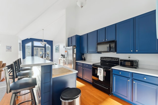 kitchen with an island with sink, black appliances, hanging light fixtures, and blue cabinetry