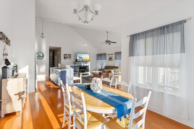 dining area featuring hardwood / wood-style flooring, sink, high vaulted ceiling, and ceiling fan with notable chandelier