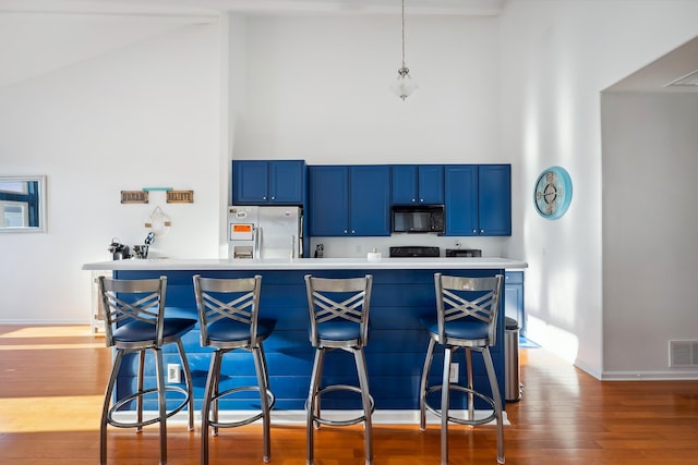 kitchen with high vaulted ceiling, stainless steel refrigerator, pendant lighting, and a breakfast bar