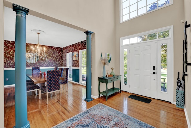 foyer entrance featuring hardwood / wood-style flooring, ornate columns, and a notable chandelier