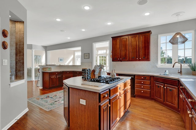 kitchen with light wood-type flooring, stainless steel gas cooktop, sink, decorative light fixtures, and a center island