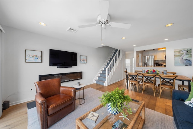 living area with recessed lighting, visible vents, light wood finished floors, and stairs