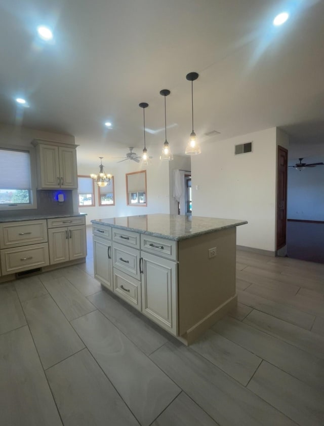 kitchen with pendant lighting, ceiling fan with notable chandelier, a kitchen island, and light stone countertops