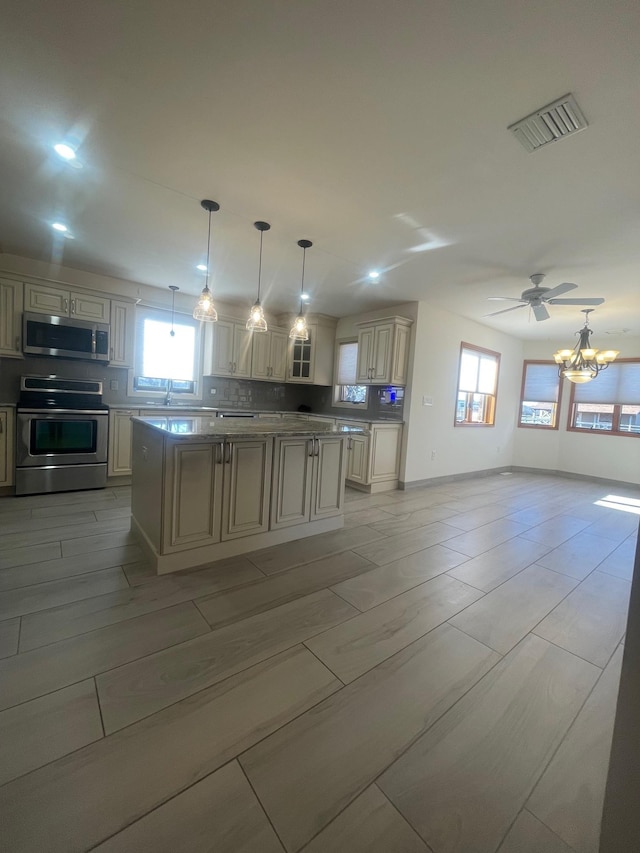 kitchen with pendant lighting, ceiling fan with notable chandelier, stainless steel appliances, and cream cabinetry