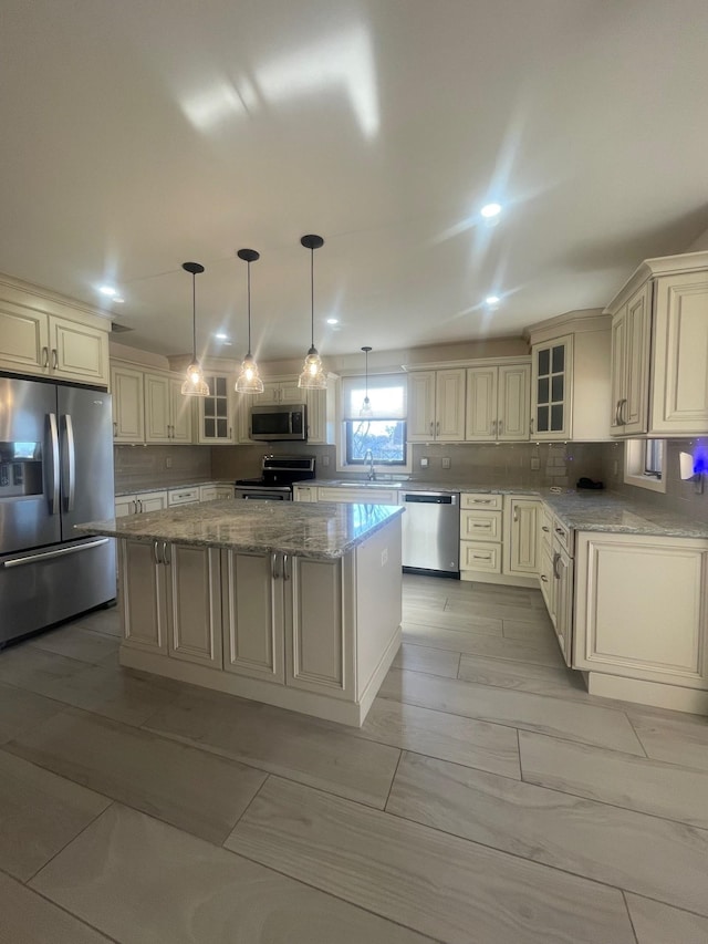 kitchen featuring light stone countertops, appliances with stainless steel finishes, decorative light fixtures, cream cabinetry, and a center island