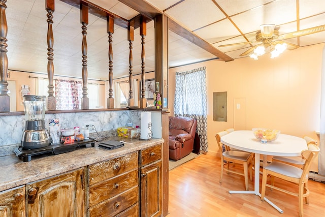 kitchen featuring a ceiling fan, electric panel, decorative backsplash, light wood finished floors, and brown cabinetry