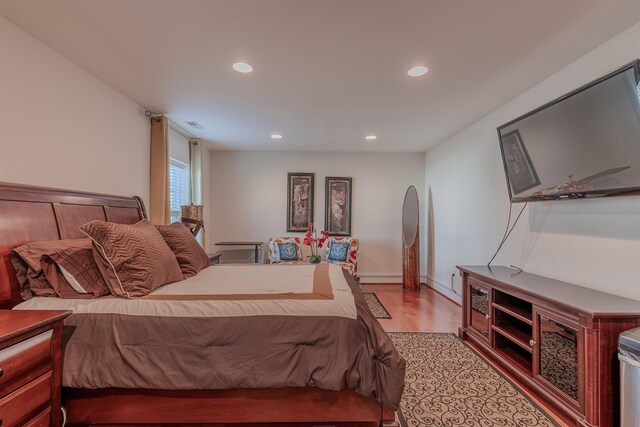 bedroom with arched walkways, a baseboard radiator, recessed lighting, visible vents, and light wood-style floors