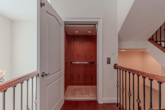 corridor featuring elevator, wood finished floors, an upstairs landing, and baseboards