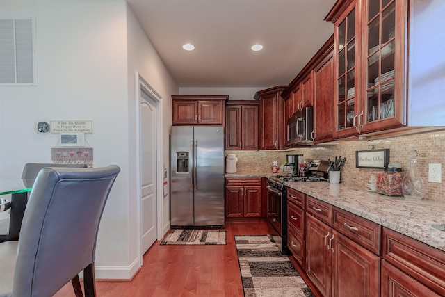 kitchen featuring appliances with stainless steel finishes, glass insert cabinets, light stone counters, and tasteful backsplash