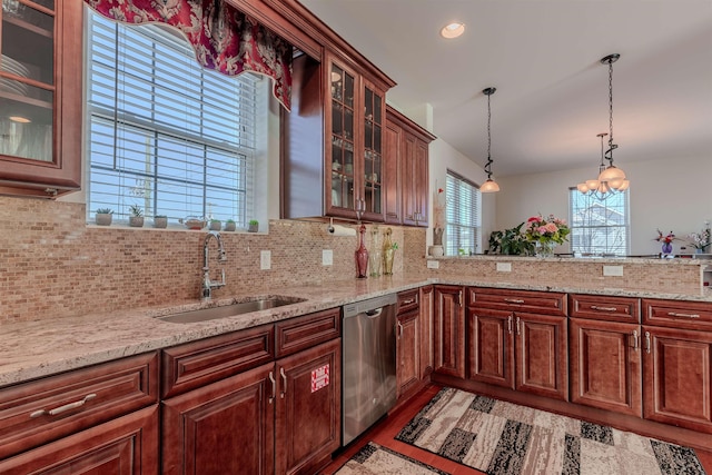 kitchen with light stone counters, hanging light fixtures, stainless steel dishwasher, glass insert cabinets, and a sink