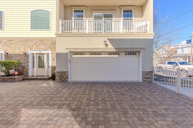 multi unit property featuring decorative driveway, stucco siding, fence, a garage, and stone siding