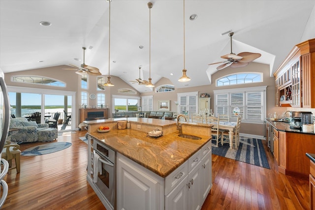 kitchen with light stone countertops, stainless steel oven, sink, a center island with sink, and white cabinetry