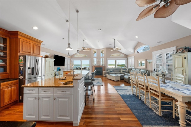 kitchen with stainless steel refrigerator with ice dispenser, sink, decorative light fixtures, a center island with sink, and white cabinets