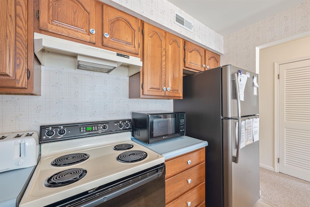 kitchen with freestanding refrigerator, wallpapered walls, under cabinet range hood, visible vents, and range with electric stovetop