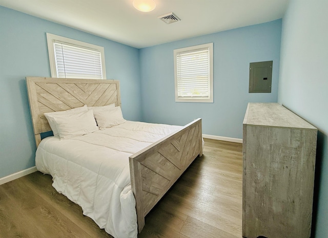 bedroom featuring baseboards, electric panel, wood finished floors, and visible vents