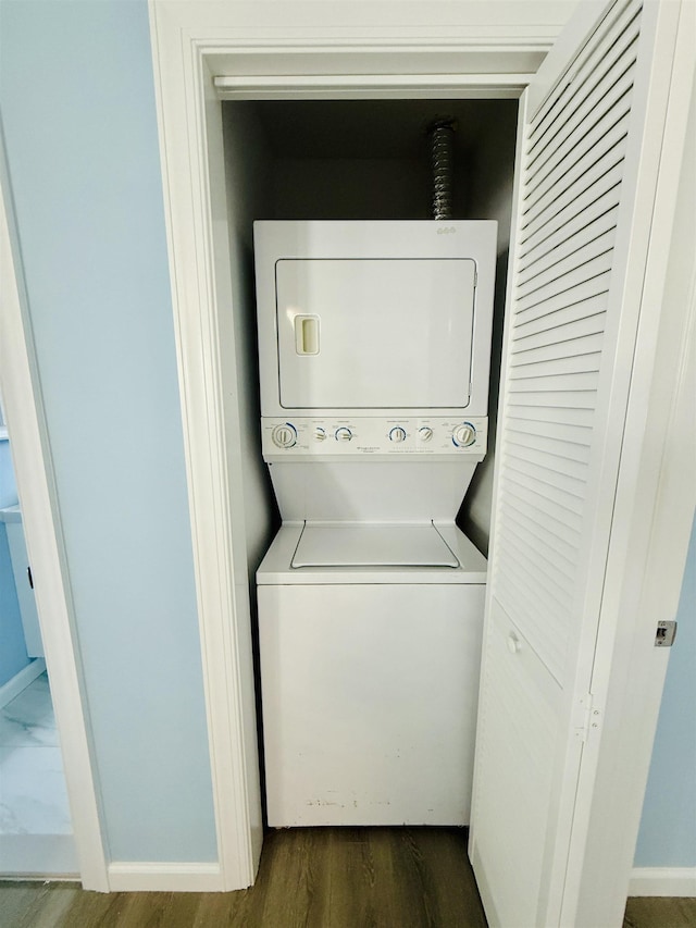 laundry area featuring laundry area, stacked washer and dryer, baseboards, and dark wood-type flooring