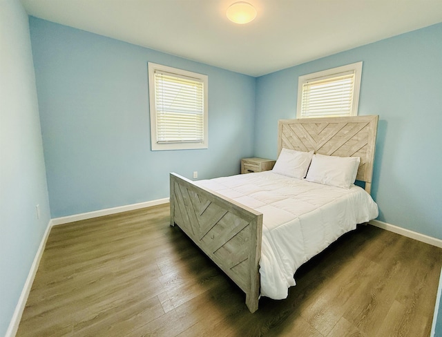 bedroom with baseboards, multiple windows, and wood finished floors