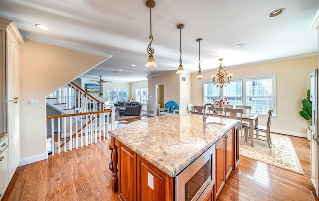 kitchen featuring stainless steel microwave, light stone counters, decorative light fixtures, and a kitchen island with sink