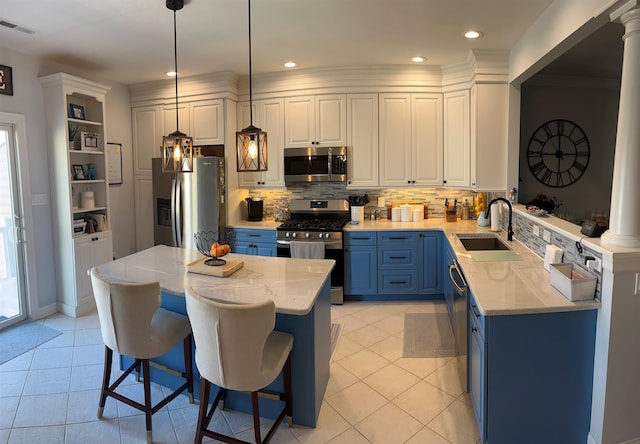 kitchen featuring stainless steel appliances, blue cabinetry, pendant lighting, sink, and decorative columns