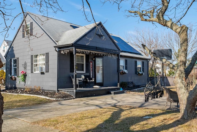 view of front of house with a porch, solar panels, and roof with shingles