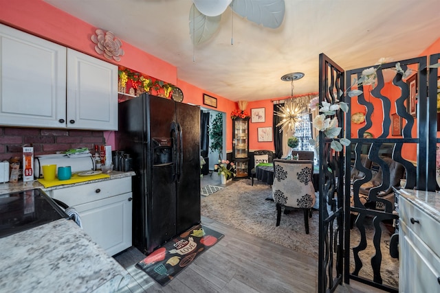 kitchen with wood finished floors, hanging light fixtures, black refrigerator with ice dispenser, white cabinetry, and ceiling fan with notable chandelier