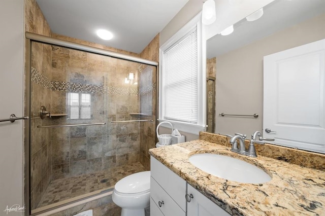 bathroom featuring toilet, a stall shower, a wealth of natural light, and vanity