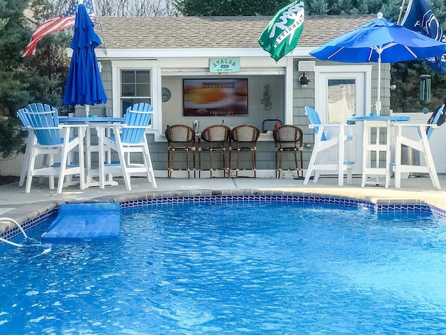 pool featuring a storage structure, a patio area, outdoor dry bar, and an outdoor structure